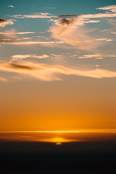 Bright cloudy sky illuminated by sunlight over sea at night